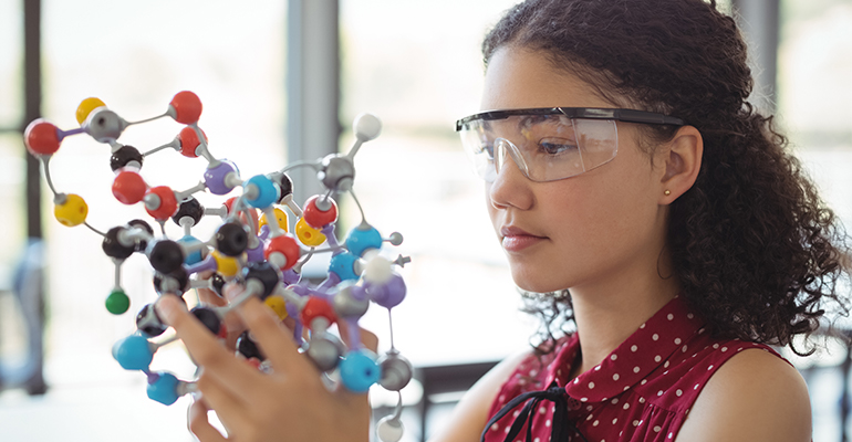 girl with safety goggles, looking at a chemistry model